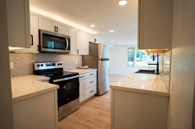 kitchen with white cabinetry, stainless steel appliances, light stone counters, backsplash, and light wood-type flooring