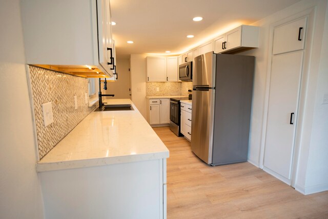 kitchen with tasteful backsplash, stainless steel appliances, sink, light hardwood / wood-style flooring, and white cabinetry