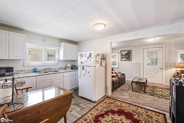 1029 Boatfield Ave, Flint, MI 48507 - kitchen with freestanding refrigerator, a sink, black microwave, light wood-type flooring, and white cabinetry