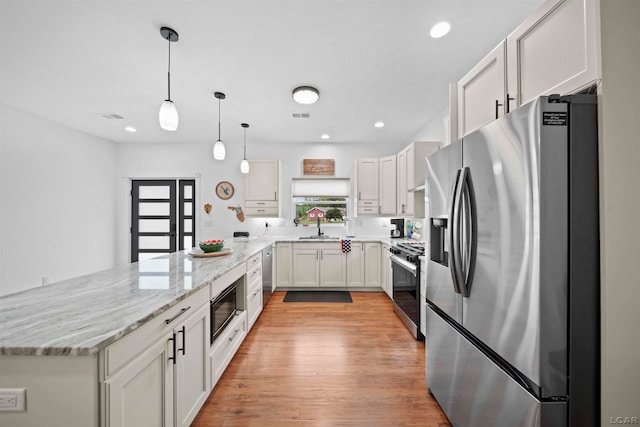 kitchen with hanging light fixtures, appliances with stainless steel finishes, light hardwood / wood-style floors, light stone counters, and white cabinetry