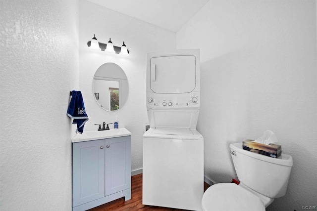 bathroom with wood-type flooring, lofted ceiling, stacked washer / drying machine, toilet, and vanity