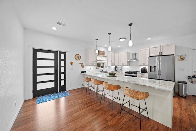 kitchen with wall chimney exhaust hood, dark hardwood / wood-style floors, appliances with stainless steel finishes, decorative light fixtures, and white cabinetry