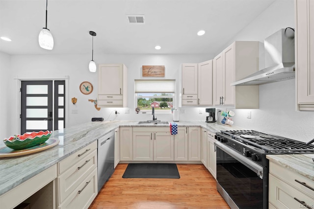 kitchen featuring light wood-type flooring, stainless steel appliances, sink, wall chimney range hood, and hanging light fixtures