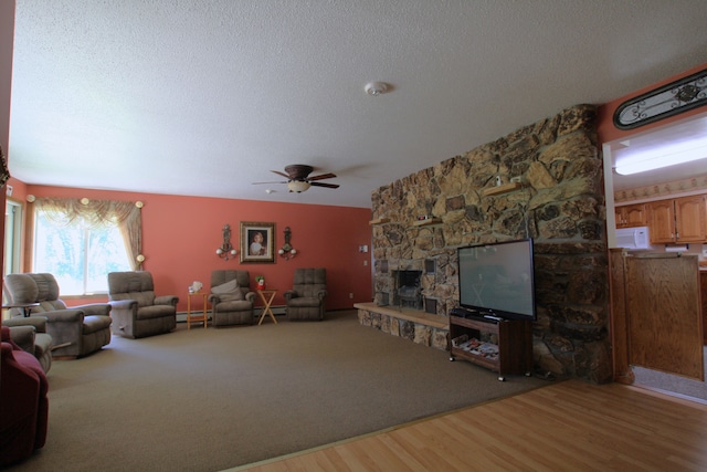 living room with ceiling fan, baseboard heating, hardwood / wood-style floors, a textured ceiling, and a fireplace