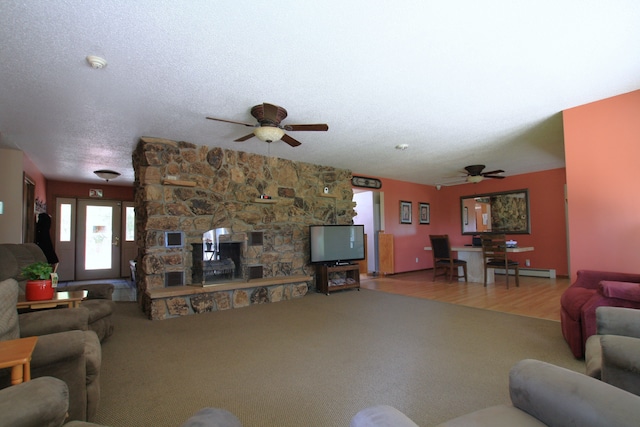 living room with ceiling fan, a baseboard radiator, a stone fireplace, hardwood / wood-style floors, and a textured ceiling