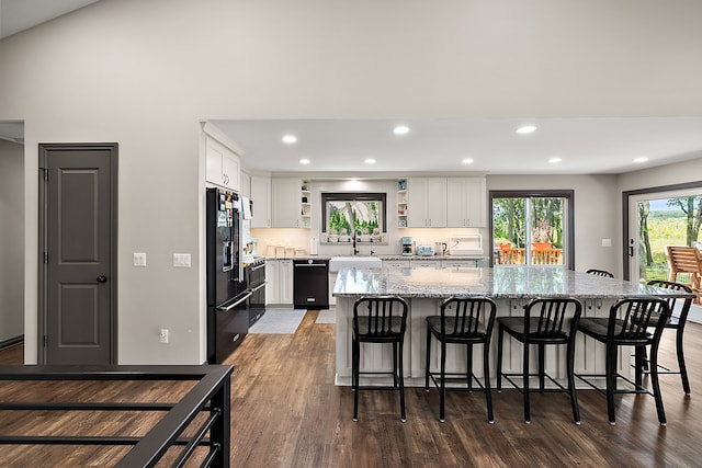 kitchen with white cabinets, a kitchen island, light stone countertops, and black appliances