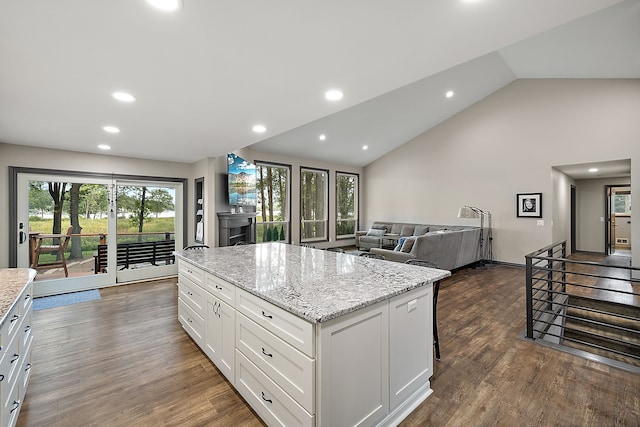 kitchen featuring white cabinetry, a center island, light stone countertops, dark hardwood / wood-style flooring, and high vaulted ceiling