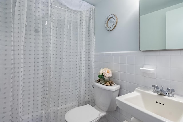 full bath featuring toilet, curtained shower, a sink, wainscoting, and tile walls