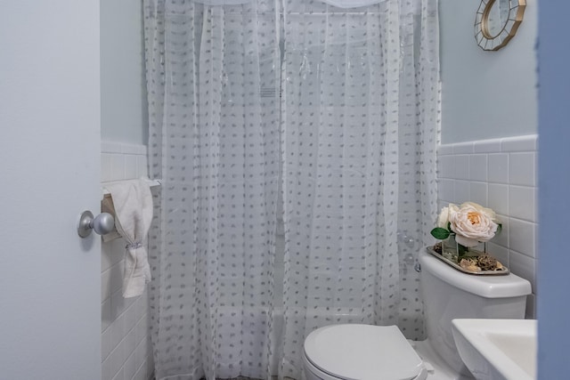 bathroom featuring a shower with curtain, toilet, a wainscoted wall, and tile walls