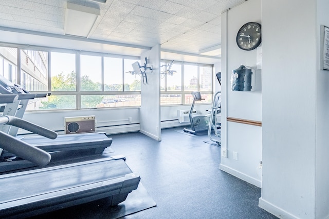 gym featuring a drop ceiling, a baseboard radiator, and baseboards