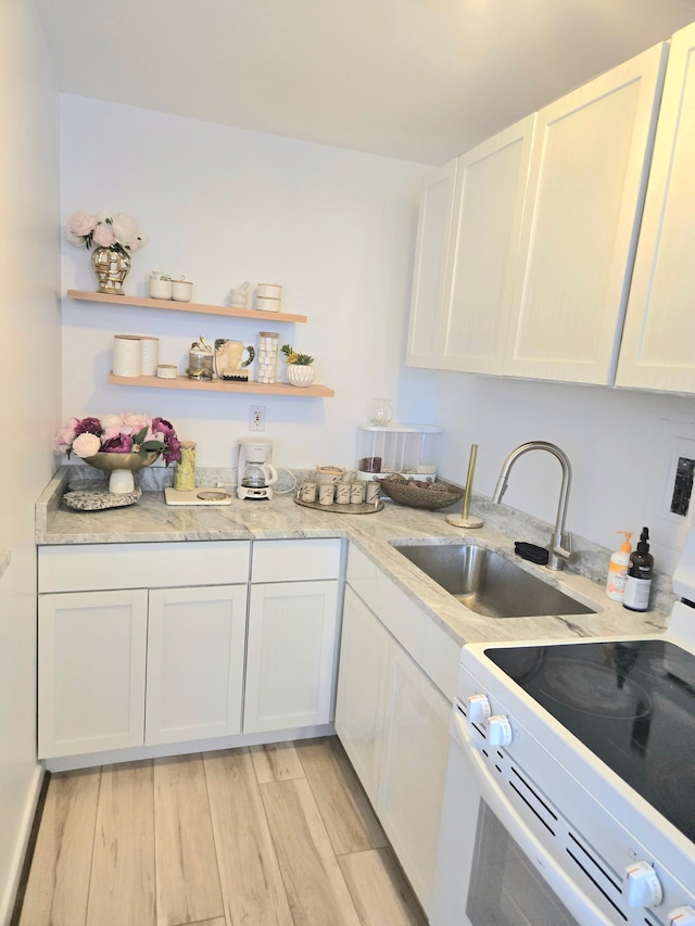 kitchen with white range with electric stovetop, white cabinets, a sink, and light wood finished floors