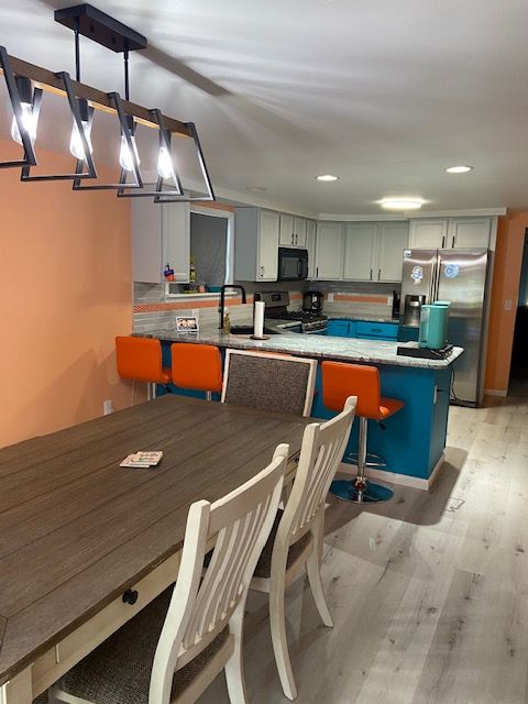 kitchen with kitchen peninsula, a kitchen bar, light wood-type flooring, backsplash, and stainless steel appliances