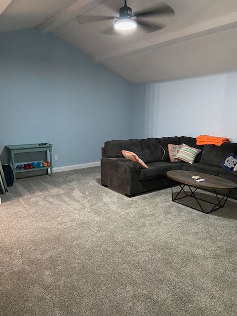 carpeted living room featuring vaulted ceiling with beams and ceiling fan