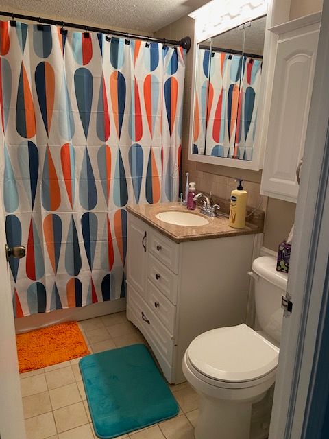 bathroom with walk in shower, tile patterned floors, a textured ceiling, toilet, and vanity