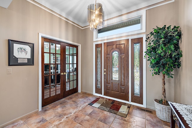 foyer entrance featuring french doors, ornamental molding, and an inviting chandelier