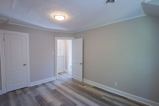 unfurnished bedroom featuring a textured ceiling, wood-type flooring, and ornamental molding