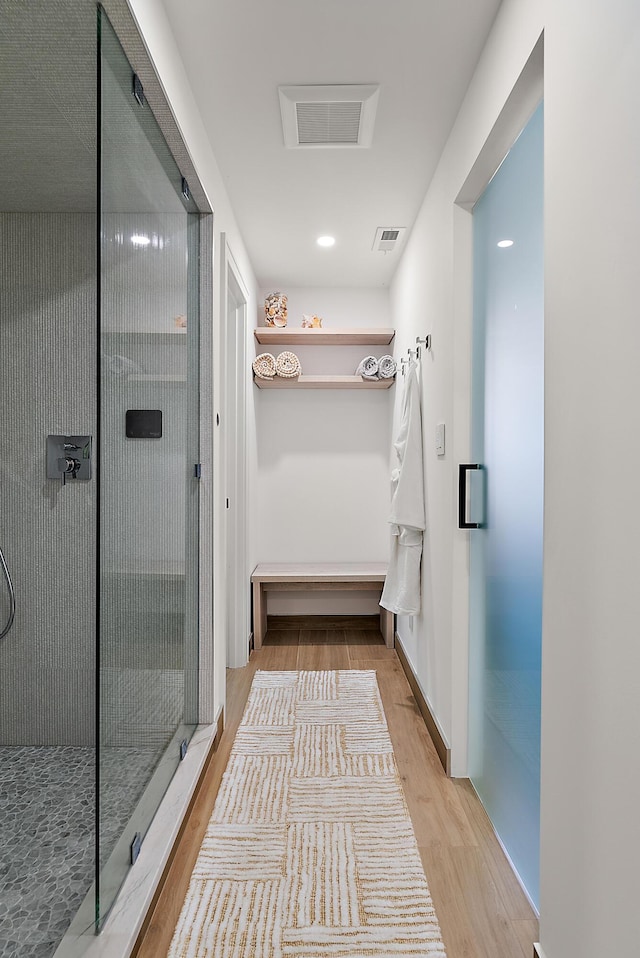 bathroom with wood finished floors, tiled shower, and visible vents