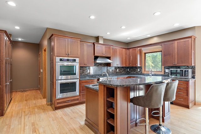 kitchen with light hardwood / wood-style flooring, backsplash, dark stone counters, a kitchen island, and appliances with stainless steel finishes