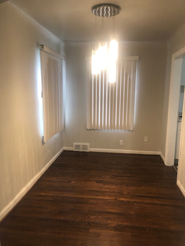 empty room with dark hardwood / wood-style flooring and an inviting chandelier