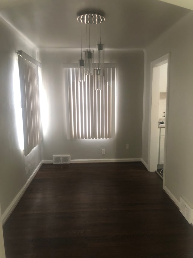 unfurnished dining area featuring dark hardwood / wood-style flooring and an inviting chandelier