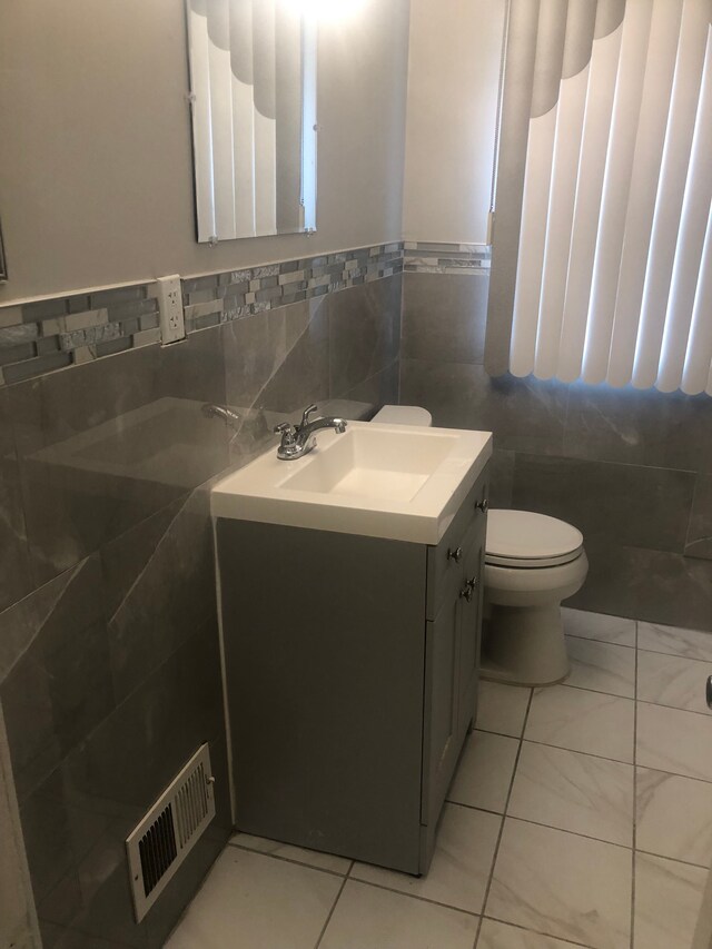 bathroom featuring tile patterned flooring, vanity, toilet, and tile walls