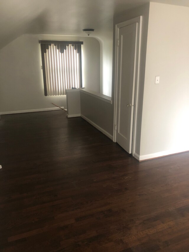 unfurnished room with vaulted ceiling and dark wood-type flooring