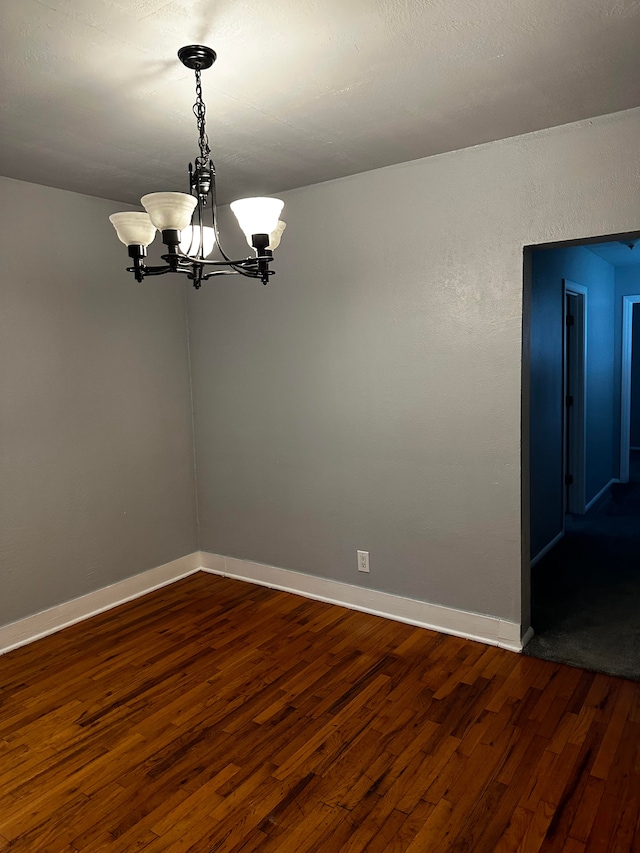 spare room with a notable chandelier and dark wood-type flooring