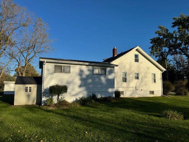 rear view of house with a storage unit and a lawn