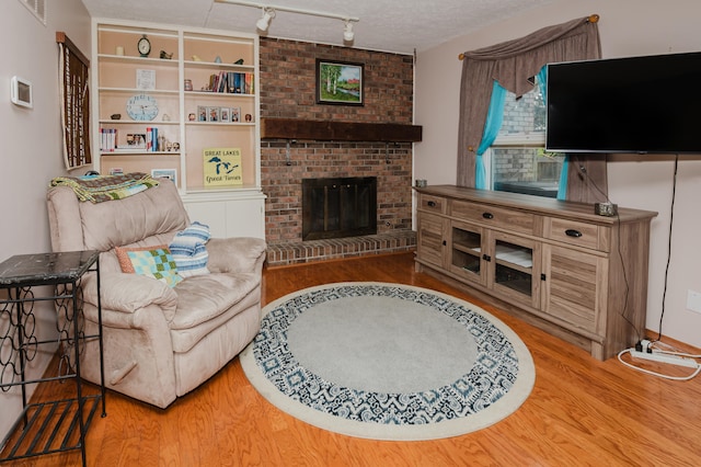 living room featuring a fireplace, a textured ceiling, rail lighting, and hardwood / wood-style flooring