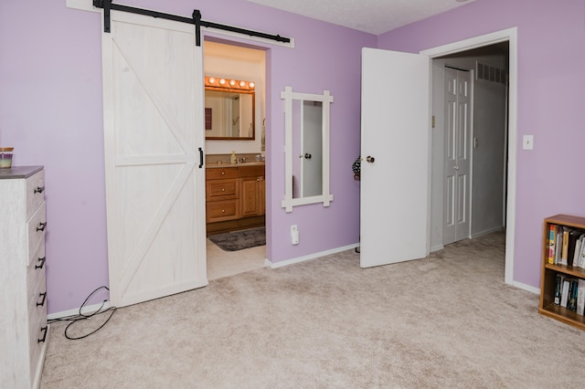 unfurnished bedroom featuring a barn door, ensuite bathroom, sink, and light carpet