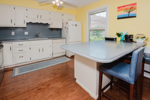 kitchen featuring a kitchen bar, tasteful backsplash, white appliances, sink, and wood-type flooring