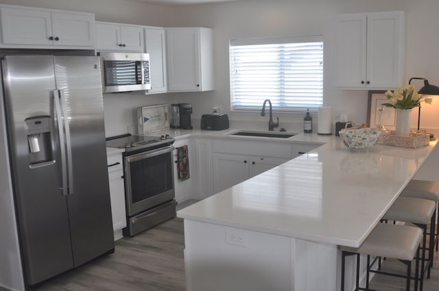 kitchen with a breakfast bar, white cabinets, sink, dark hardwood / wood-style floors, and stainless steel appliances