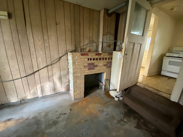 misc room with concrete flooring, a brick fireplace, wooden walls, and water heater