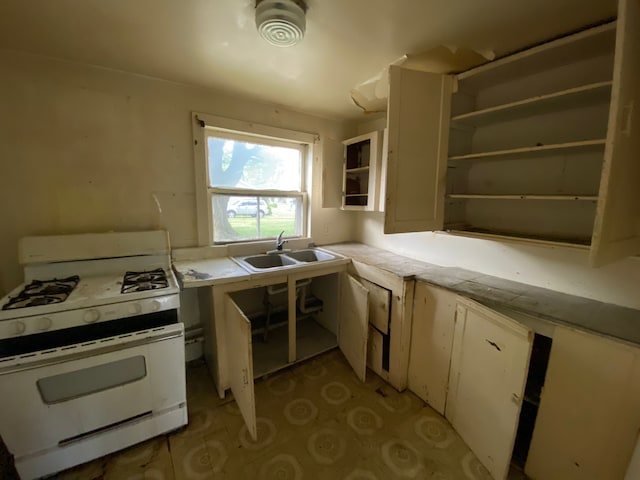 kitchen featuring white gas range, white cabinetry, sink, and tile countertops