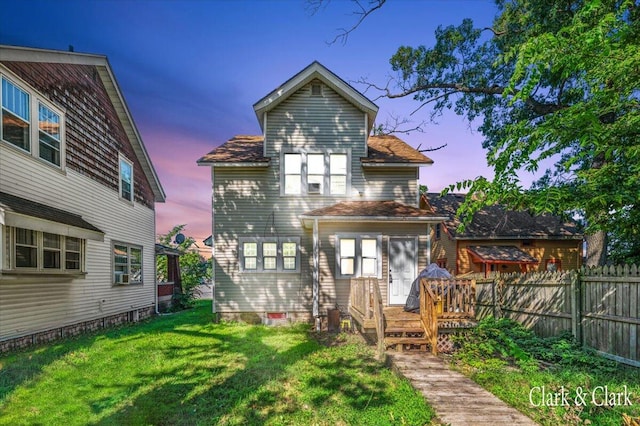 back house at dusk with a lawn and a deck