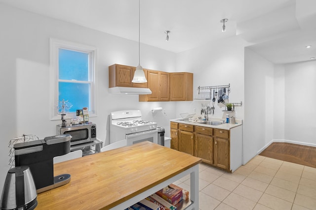 kitchen with light tile patterned floors, hanging light fixtures, gas range gas stove, and sink