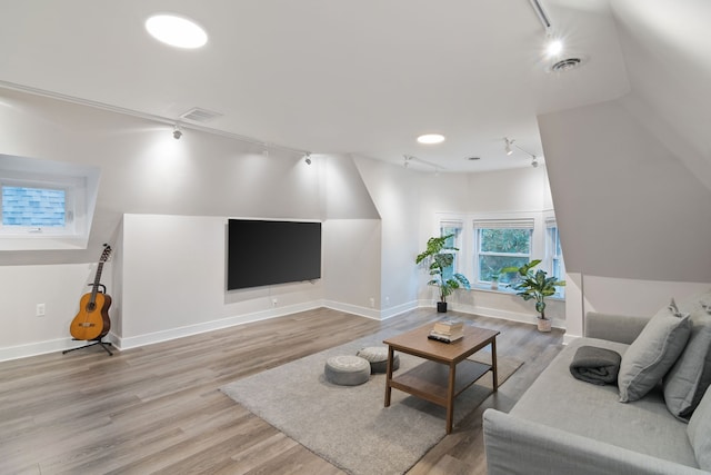 living room featuring rail lighting, light hardwood / wood-style floors, and lofted ceiling