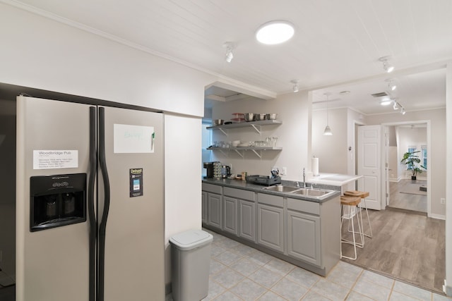 kitchen with gray cabinetry, sink, stainless steel refrigerator with ice dispenser, light hardwood / wood-style floors, and a breakfast bar