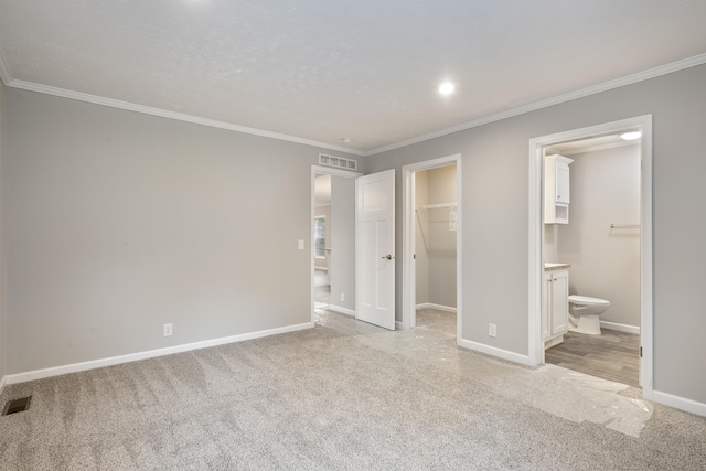 unfurnished bedroom with light carpet, ensuite bathroom, a walk in closet, crown molding, and a closet