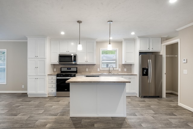 kitchen with sink, stainless steel appliances, pendant lighting, white cabinets, and ornamental molding