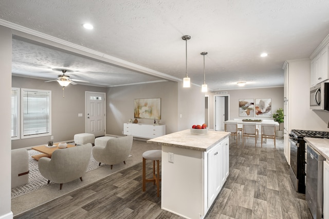 kitchen with appliances with stainless steel finishes, hardwood / wood-style flooring, a center island, white cabinetry, and hanging light fixtures