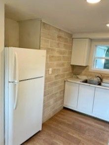 kitchen with sink, white fridge, light hardwood / wood-style floors, white cabinetry, and brick wall