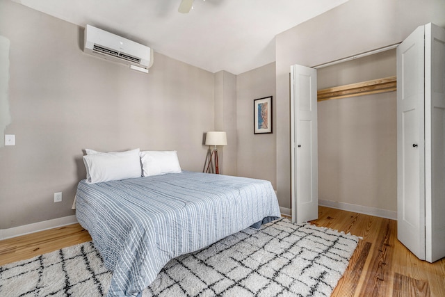 bedroom featuring ceiling fan, light hardwood / wood-style floors, an AC wall unit, and a closet