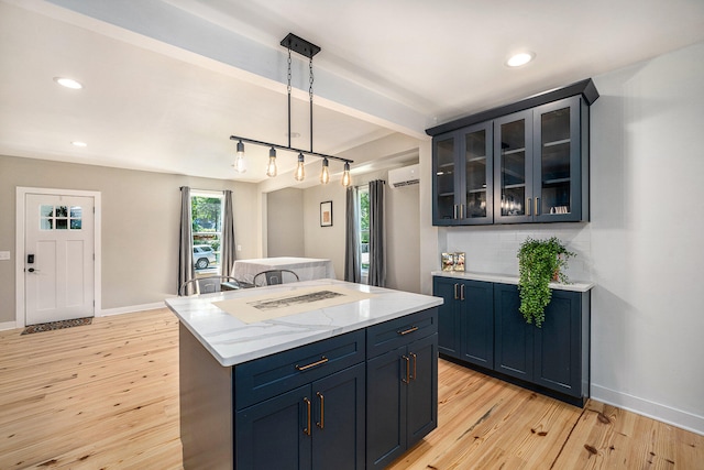 kitchen with pendant lighting, a wall mounted air conditioner, light stone countertops, and light hardwood / wood-style flooring