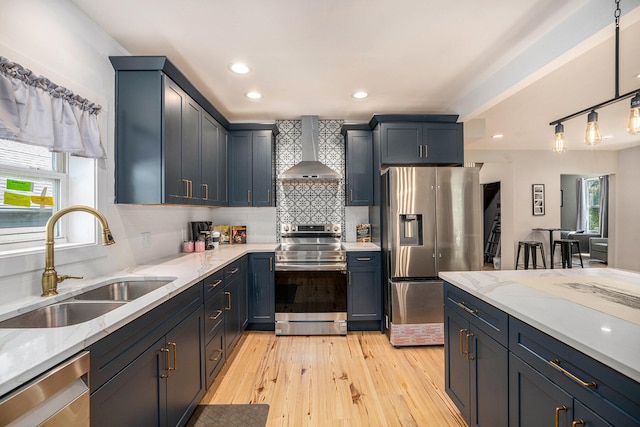 kitchen featuring sink, wall chimney exhaust hood, hanging light fixtures, stainless steel appliances, and light hardwood / wood-style floors