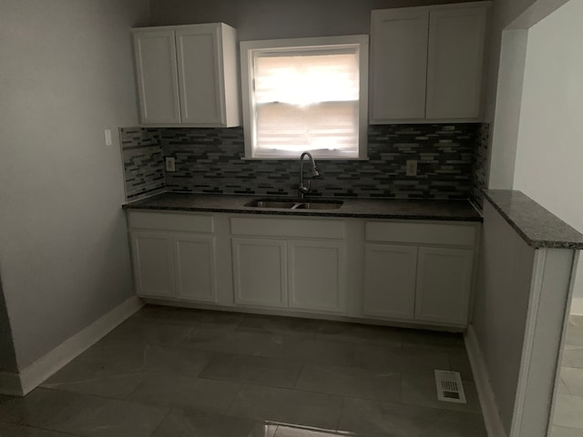 kitchen with dark stone counters, white cabinets, sink, dark tile patterned floors, and tasteful backsplash