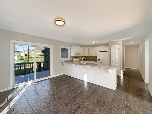 kitchen featuring a kitchen bar, kitchen peninsula, light stone countertops, white appliances, and white cabinets