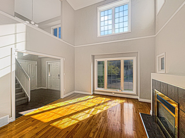 unfurnished living room featuring wood-type flooring, a towering ceiling, and a tiled fireplace