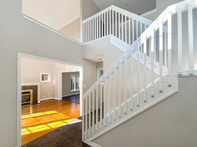 staircase with a tile fireplace, wood-type flooring, and a towering ceiling