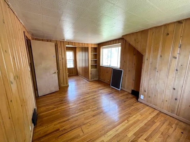 additional living space featuring light wood-type flooring, built in features, and wooden walls